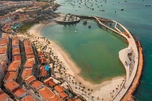 Luchtbeeld van een kustgebied met een strand, een brug en gebouwen met rode daken.
