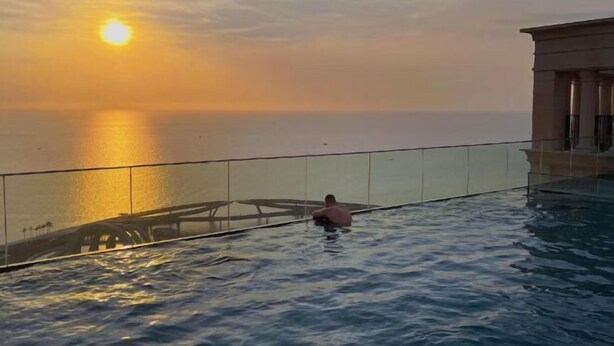 Une personne nage dans une piscine à débordement, avec une vue sur le coucher du soleil.
