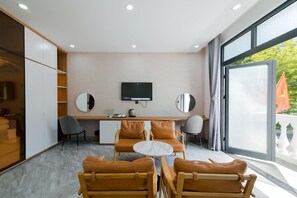 A modern hotel room with a large window, a flat-screen TV, a desk with chairs, and a seating area with a marble table. - Lalisa Hotel (Phu Quoc)