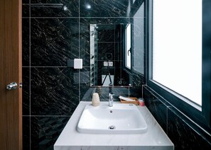 A modern bathroom with a white sink, black marble walls, and a large mirror. - Lalisa Hotel (Phu Quoc)