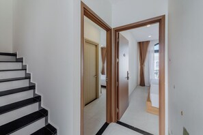 A hallway with a staircase, wooden doors, and a view into a room with a bed and curtains.