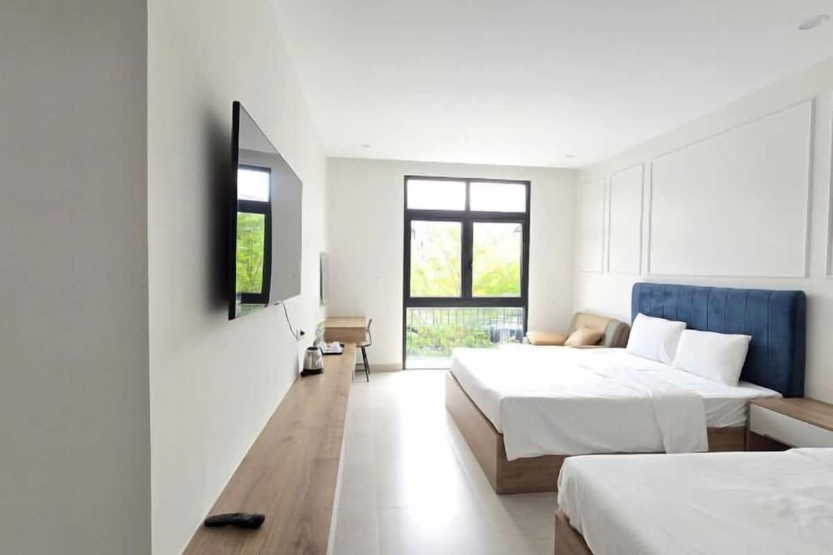 A modern hotel room with a large window, a flat-screen TV mounted on the wall, and two beds with white bedding.