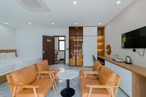 A hotel room with a bed, a desk with a TV, a seating area with chairs, and a view of the outside. - Lalisa Hotel (Phu Quoc)