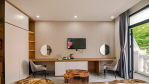 Ein modernes Hotelzimmer mit Schreibtisch, zwei Stühlen, einem Fernseher und einem großen Fenster mit Vorhängen.