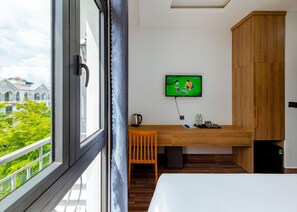 A hotel room with a large window, a wooden desk, a television, and a bed. - Lalisa Hotel (Phu Quoc)