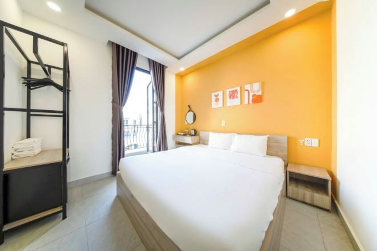 A hotel room with a large bed, a built-in shelf with towels, a bedside table, and a view of the outdoors.
