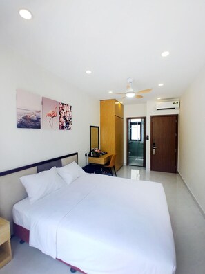 A bedroom with a bed, a desk, a chair, a ceiling fan, and a door. - Lalisa Hotel (Phu Quoc)