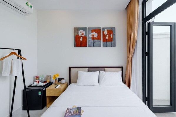 A hotel room with a bed, a nightstand, a desk, a chair, a coat rack, and a window with curtains.