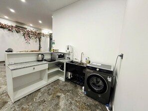 A compact kitchen with a microwave, kettle, sink, and a washing machine.