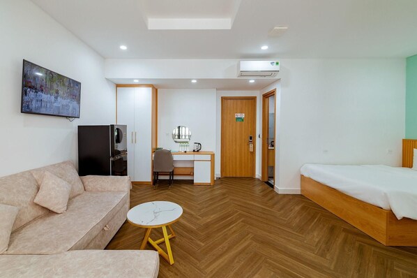 A hotel room with a bed, a sofa, a desk with a chair, a small round table, and a television.