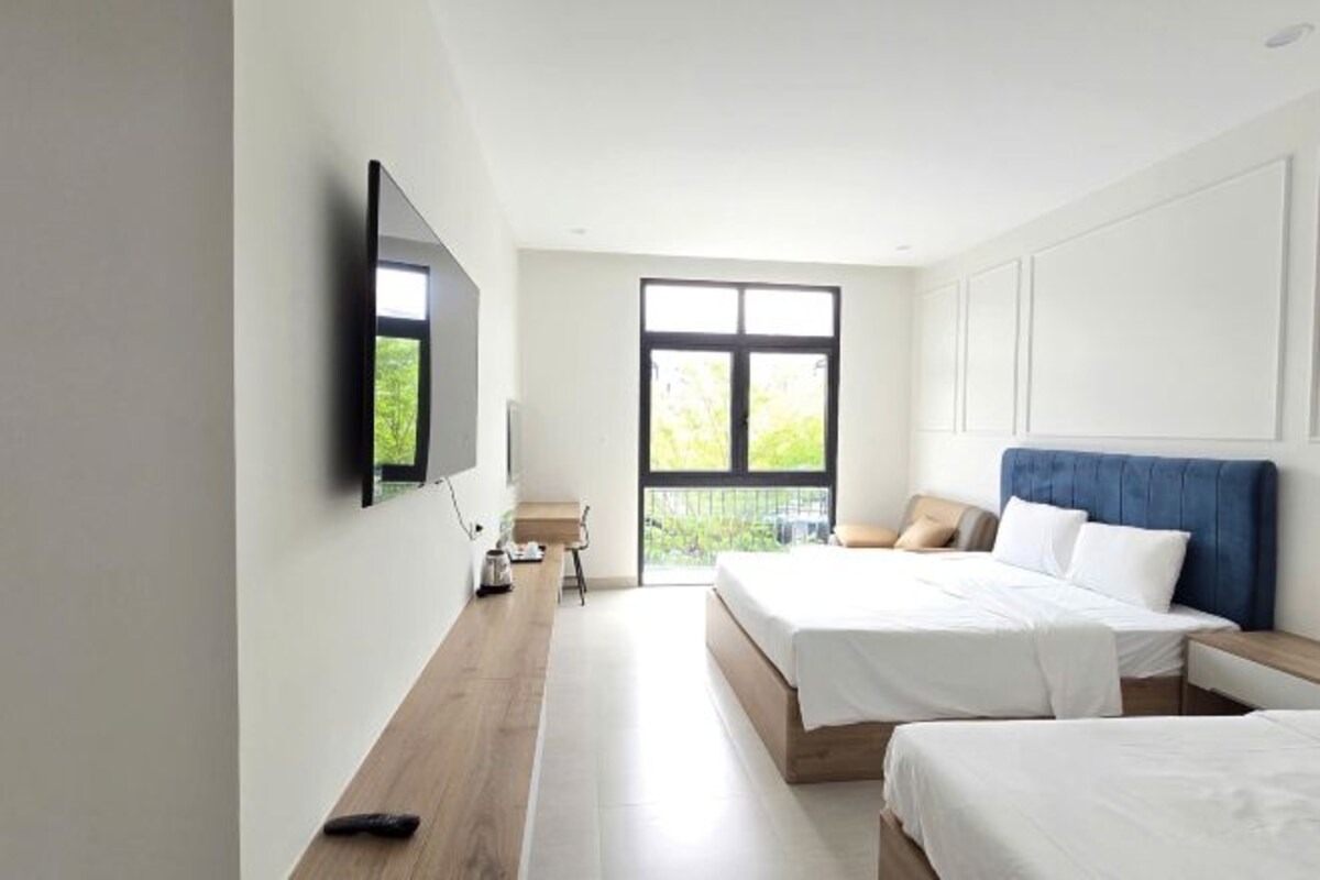 A modern hotel room with a large window, a flat-screen TV mounted on the wall, and two beds with white bedding.