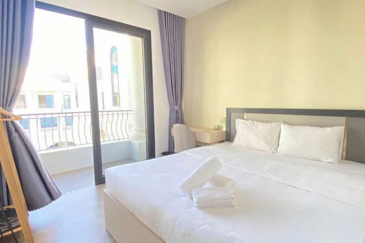 A hotel room with a bed, a desk, a chair, and a view of the outside.