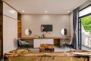 A modern hotel room with a desk, two chairs, a television, and a large window with curtains.