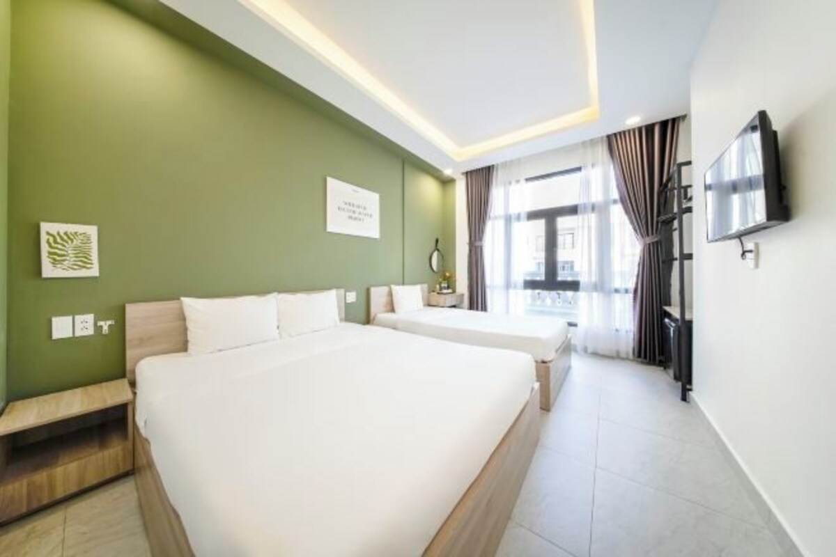 A hotel room with two beds, a flat-screen TV, a desk, and a window with curtains.