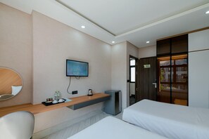 A hotel room with a bed, a desk with a computer, a TV mounted on the wall, and a small trash bin. - Lalisa Hotel (Phu Quoc)