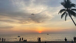 A beach with people, boats, and a sunset.