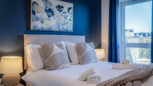 Un lit bien fait, avec des oreillers, une couverture et une serviette, une lampe de chevet et un tableau accroché au mur.
