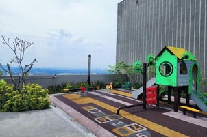 Un patio de juegos en la azotea con un tobogán y estructuras para escalar, rodeado de vegetaci ón y vistas a la ciudad.