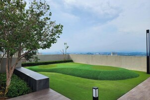Un jardín en la azotea con césped cuidado, un árbol y vistas de la ciudad.