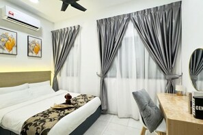 A hotel room with a bed, a desk, and a chair. There are curtains on the windows, and an air conditioner is mounted on the wall. - Nilai Vision City 4+1 PAX Akasia Suite (Nilai)