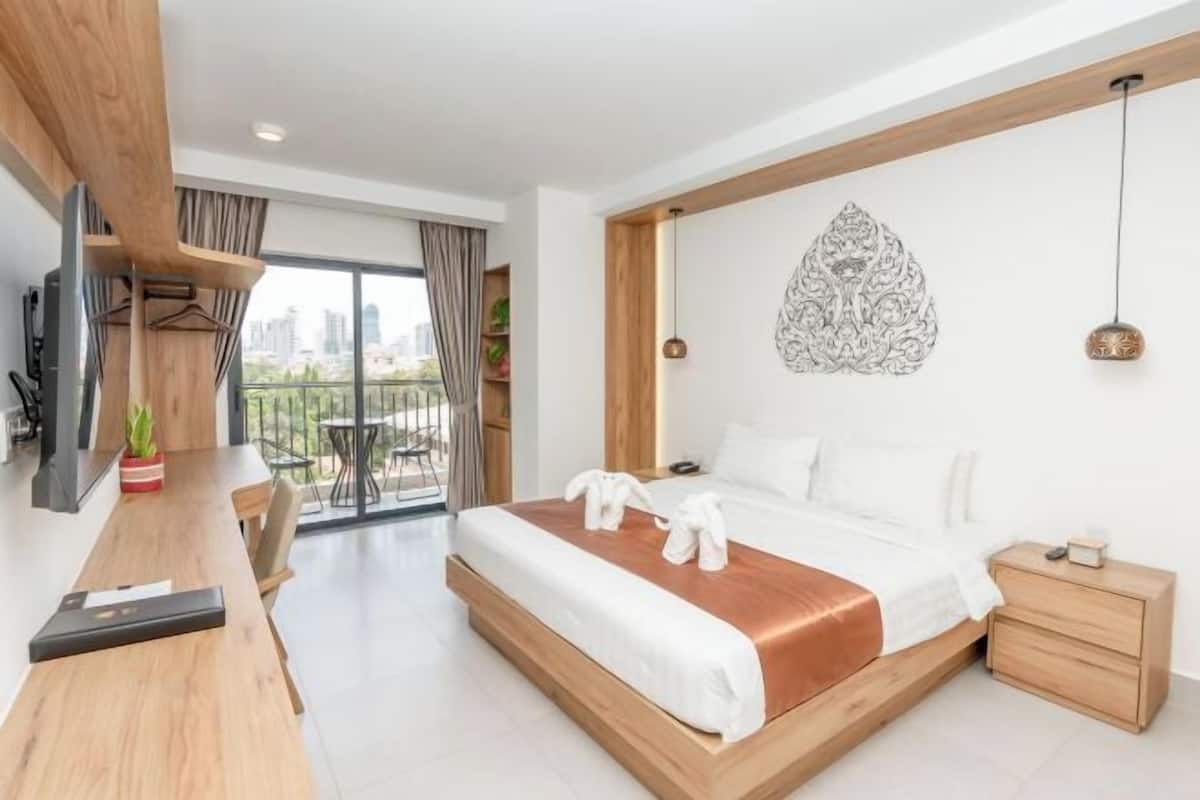 A modern hotel room with a large bed, a wooden desk, a city view, and a decorative wall piece.