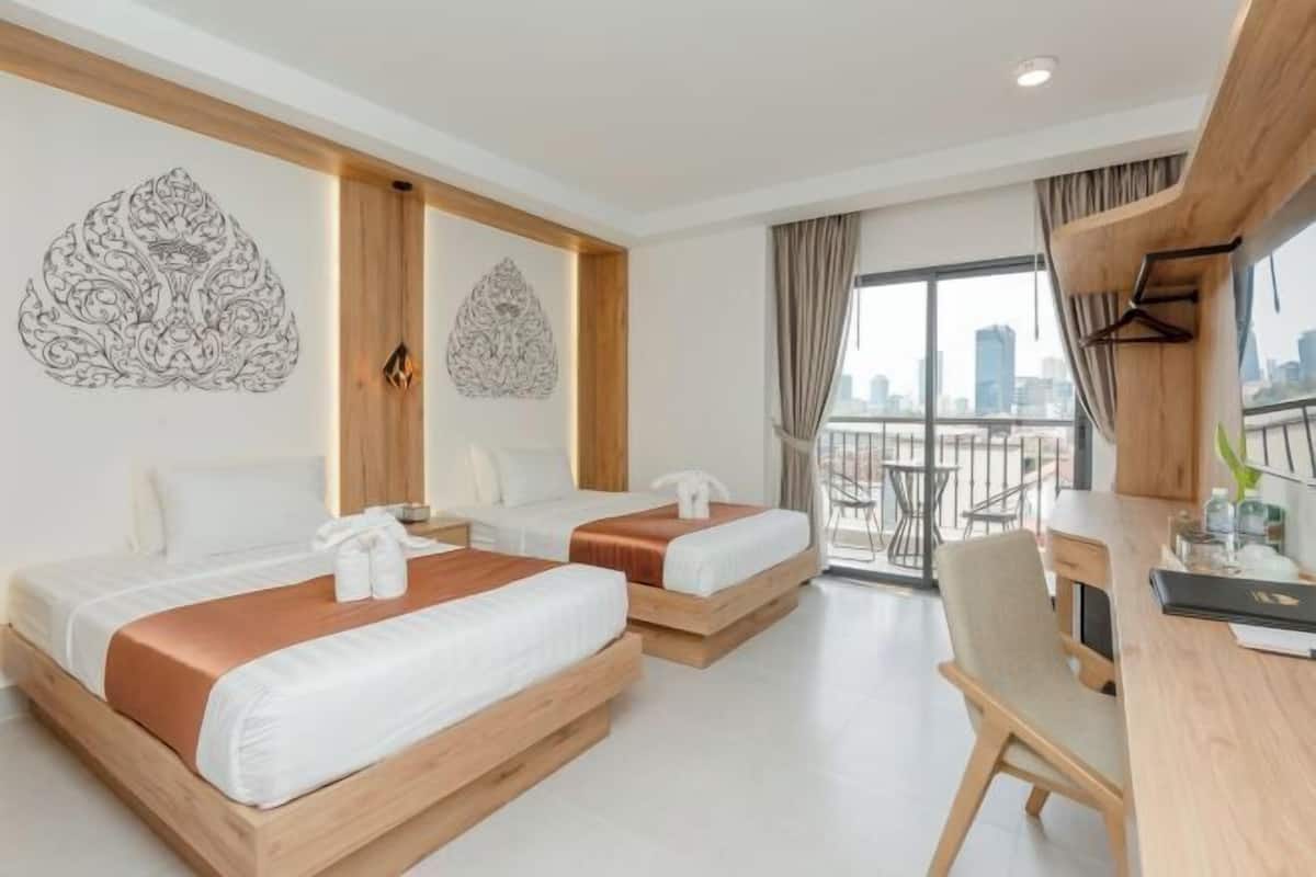 A hotel room with two beds, a desk, and a balcony with a city view.