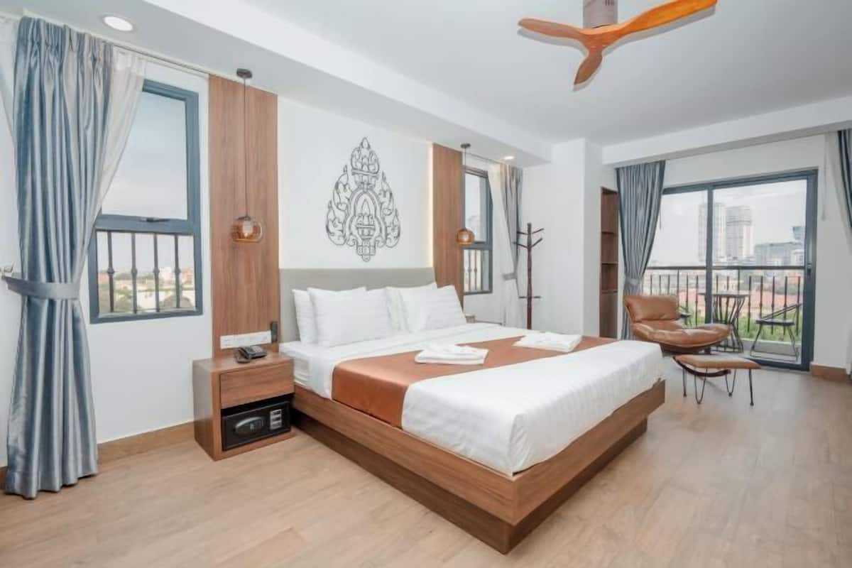 A modern hotel room with a large bed, a desk, a chair, and a balcony with a view.