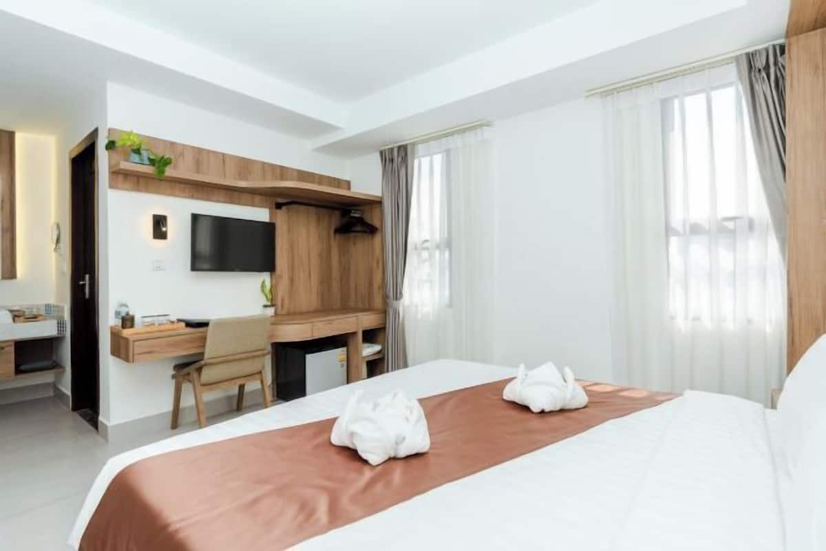 A hotel room with a bed, a desk, a chair, a TV, and a window with curtains.