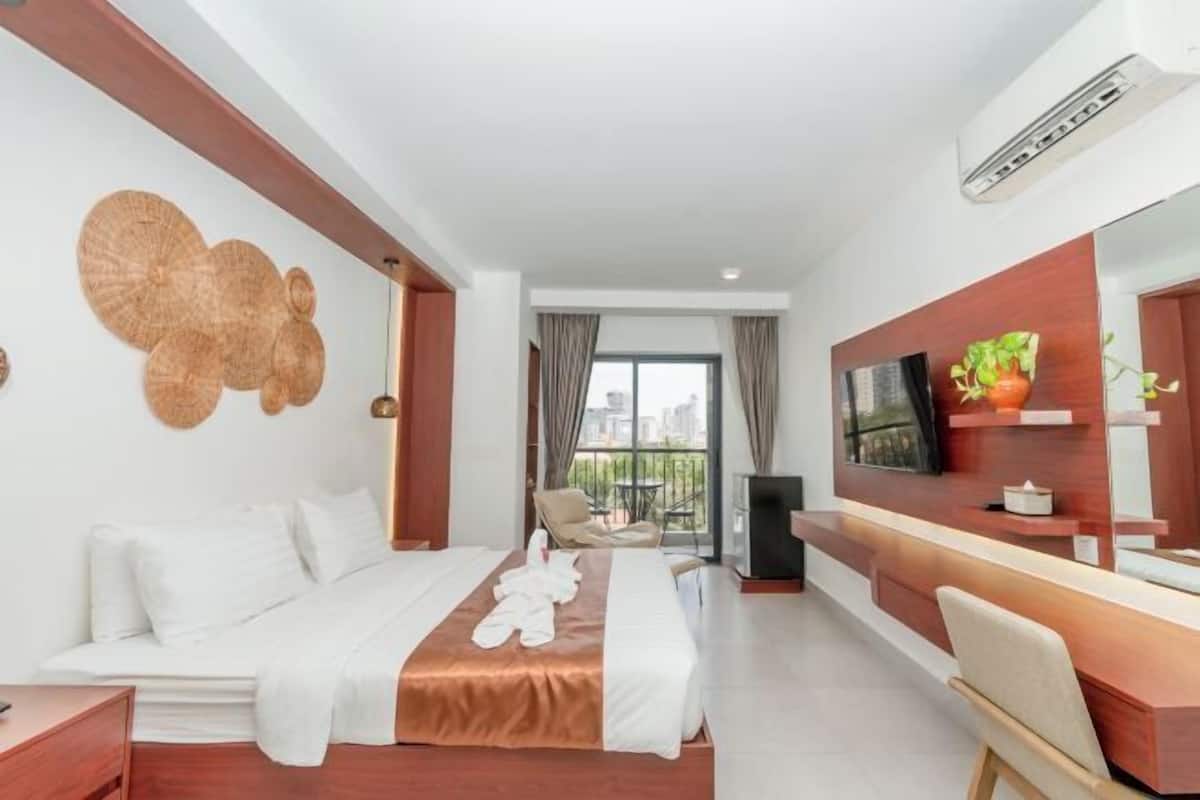 A hotel room with a bed, a desk, a chair, a TV, and a balcony with a city view.