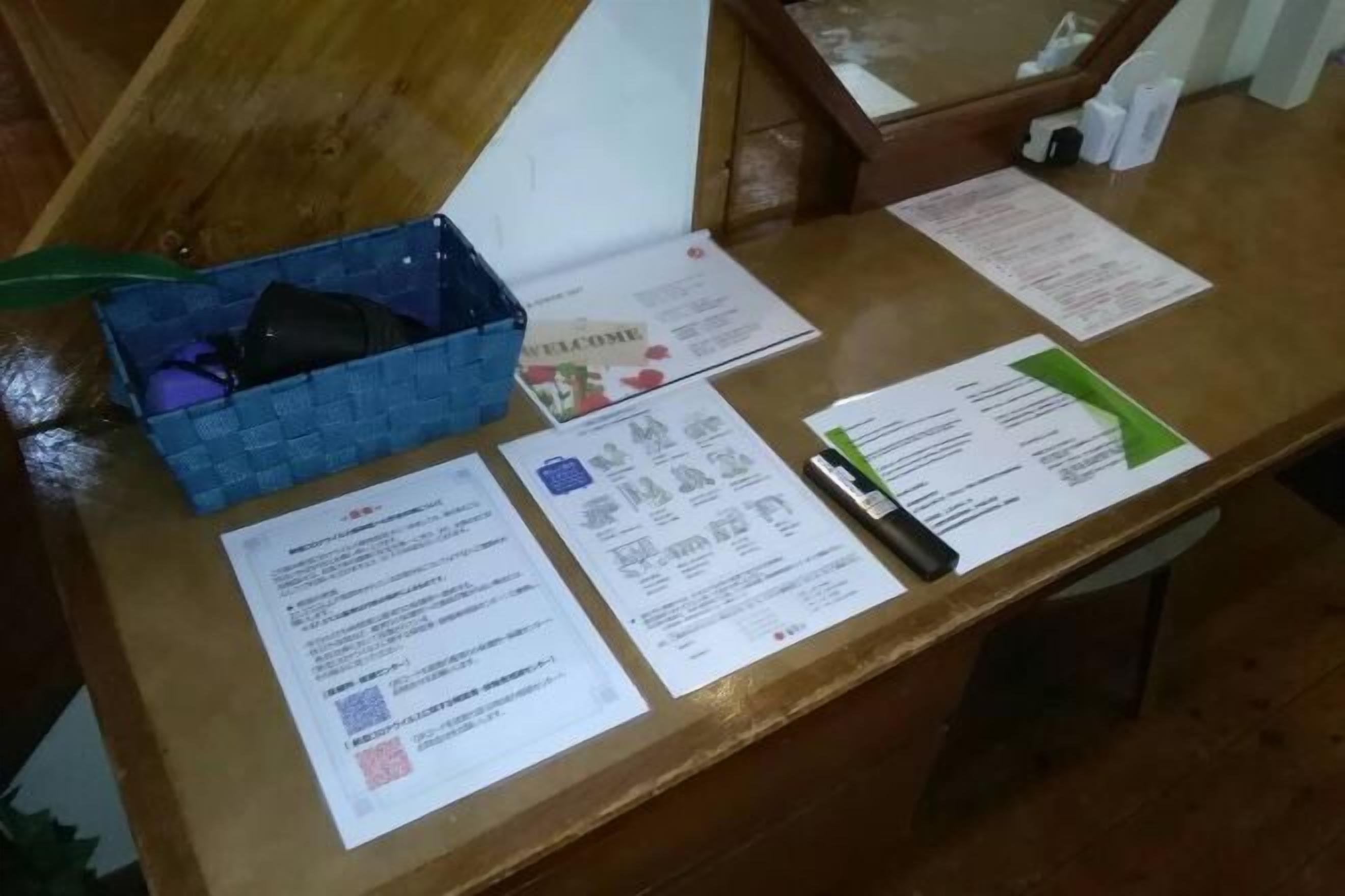 Um balcão de atendimento de madeira com diversos documentos, uma cesta azul e uma pasta verde.
