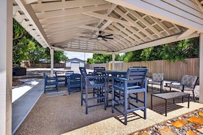 Un patio exterior con pérgola, zona de estar y una pequeña mesa.