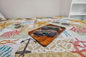 Una cama con un edredón colorido y una bandeja de madera con dos objetos negros.