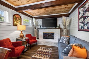 A cozy living room with a fireplace, red and grey sofas, a wooden ceiling, and a mounted television. - POOL HOT TUB! Entertainment & Location- Something for Everyone! (Long Beach)