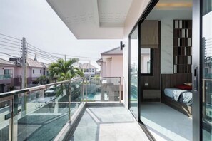 A modern balcony with a glass railing overlooking a swimming pool and neighboring buildings. - Pattaya detached four-bedroom five-bed room pool villa (Pattaya)