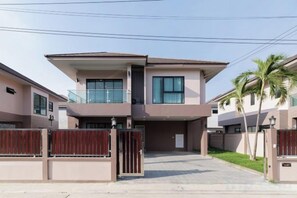 Una casa moderna de dos pisos con entrada protegida por un portón, un balcón en el nivel superior y un camino de acceso a la puerta principal.