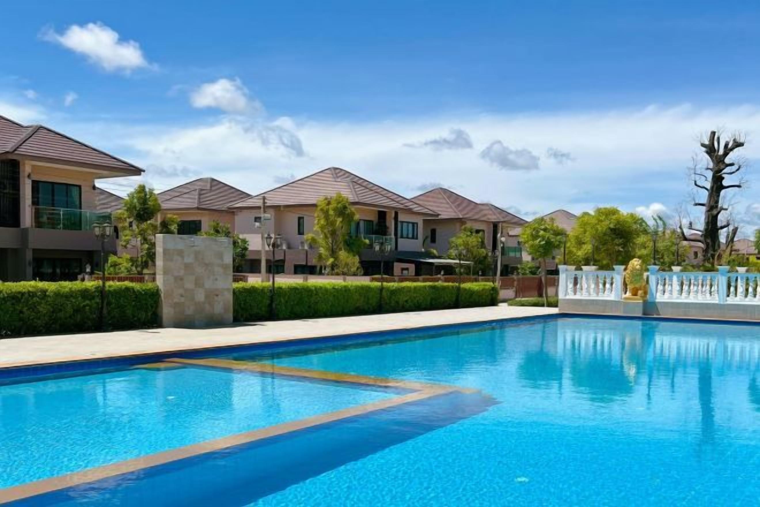 A swimming pool with a clear blue water surface, surrounded by a fence, and adjacent to a row of modern houses with flat roofs.