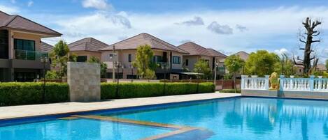 A swimming pool with a clear blue water surface, surrounded by a fence, and adjacent to a row of modern houses with flat roofs.
