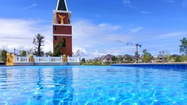 A swimming pool with clear blue water, a white fence, and a tall building with a green roof in the background. - Pattaya detached four-bedroom five-bed room pool villa (Pattaya)