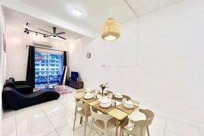 A modern living room with a dining area, a ceiling fan, a hanging light fixture, and a view through a large window. - Puchong SkyPod Residence 1-10pax next to IOI Mall Wi-Fi MRT (Puchong)