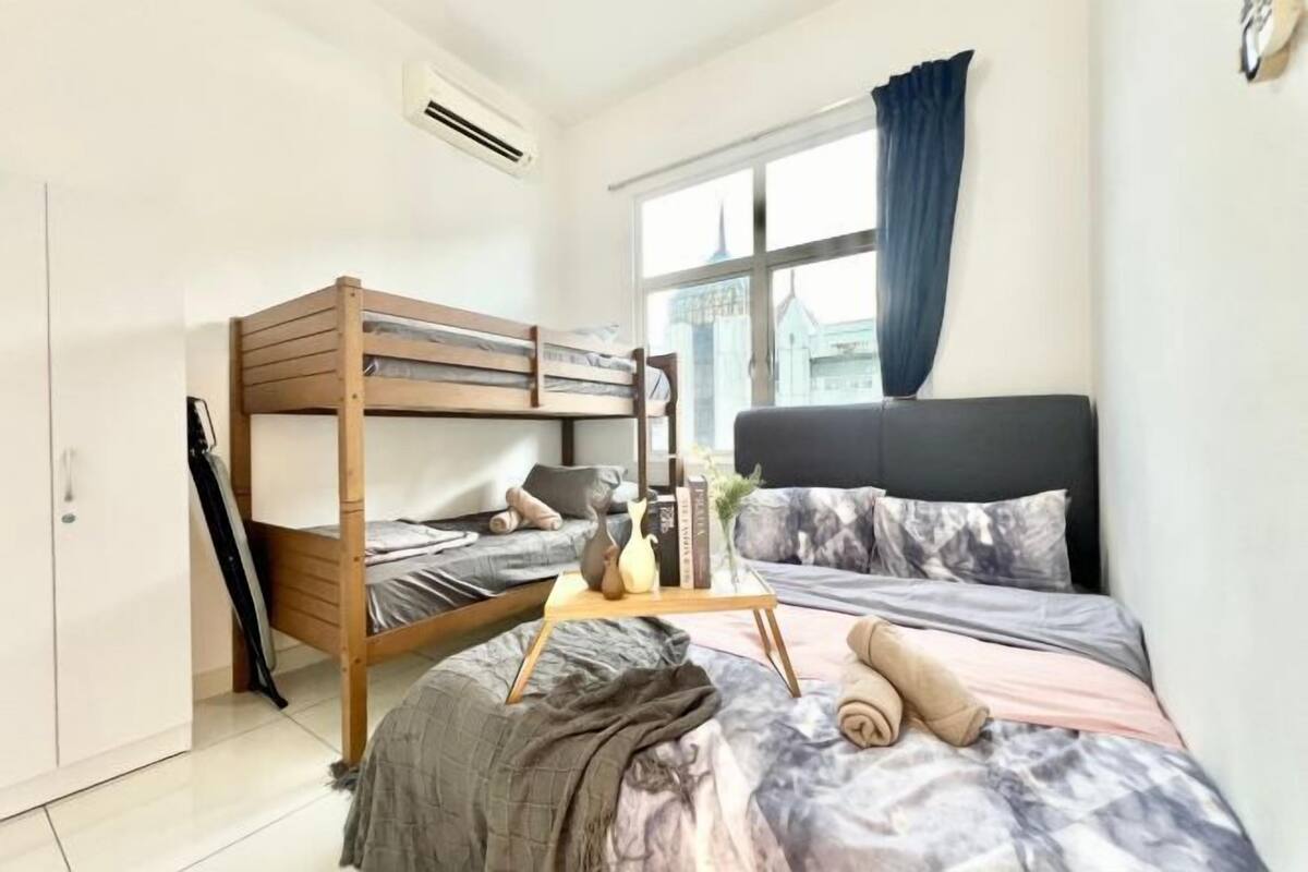 A bedroom with a bunk bed, a single bed, a bedside table with a vase, and a window with curtains.