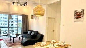 A modern living room with a black sofa, a dining table set with white plates and cups, a large window with a view of buildings, and a ceiling fan. - Puchong SkyPod Residence 1-10pax next to IOI Mall Wi-Fi MRT (Puchong)