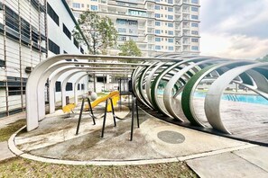 Un espace de jeux extérieur avec un toboggan jaune et des balançoires, entouré d’un bâtiment moderne au design incurvé.