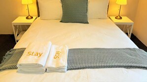 Habitación de hotel con una cama bien hecha, dos lámparas de noche, una almohada verde y toallas con la palabra "Stay".