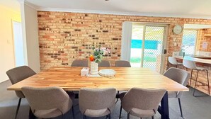 Un comedor con mesa de madera, seis sillas, un jarrón decorativo y una pared de ladrillo.