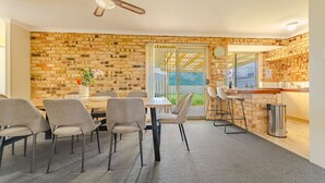 Un comedor con pared de ladrillo, ventilador de techo y mostrador de cocina con taburetes.