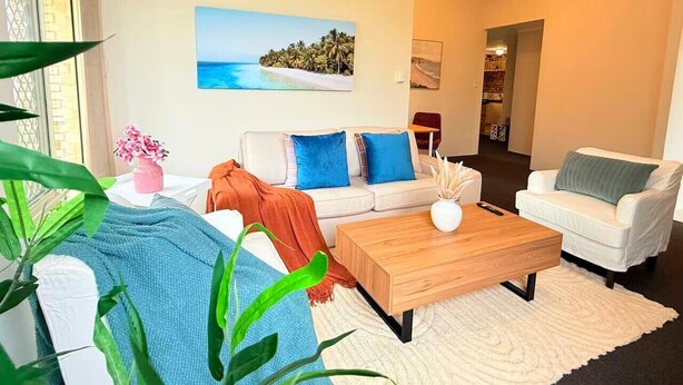Una sala de estar con un sofá blanco, una mesa de centro de madera y un cuadro de una playa.