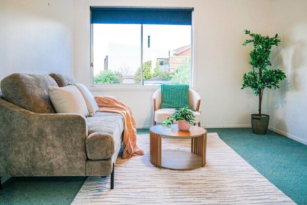 A living room with a sofa, a chair, a coffee table, and a potted plant.