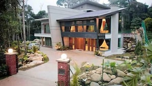 Una casa moderna de dos pisos con un sendero de piedra que conduce a la entrada, rodeada de exuberante vegetación.