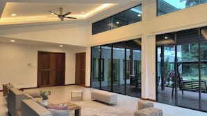 Amplia sala de estar con techo alto, ventanas grandes y ventilador de techo.