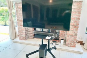 A television on a stand in a room with a brick wall and a tiled floor. - Deco Home Mesilau Golf Bungalow @ Kundasang (Kundasang)